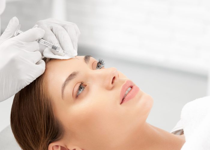 Side view of beautician in white rubber gloves holding syringe and doing special beauty injection in skin face. Concept of professional procedures and cosmetics for improvements skin.