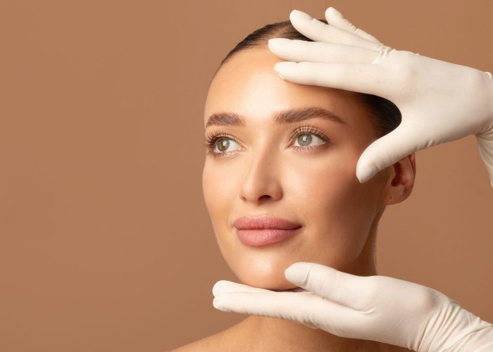 Cosmetic surgery concept. Doctor examining young woman's face, beautiful lady during visit to cosmetologist cabinet, beige studio background, copy space